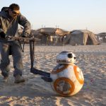 Puppeteer Brian Herring, dressed in a grey greenscreen suit and goggles, operates the BB-8 droid puppet across a sandy desert set during the filming of the Star Wars sequel trilogy.