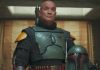 A medium shot of Temuera Morrison as Boba Fett, wearing his green and black Beskar armor without a helmet, standing in his palace on Tatooine.