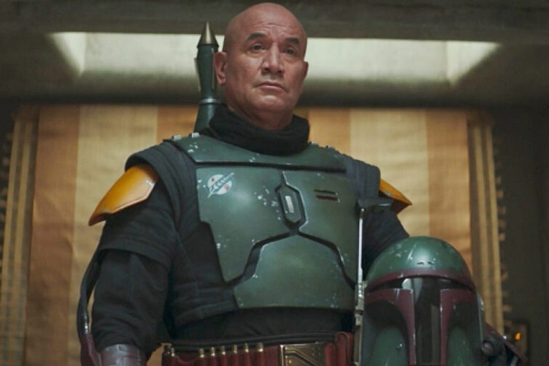 A medium shot of Temuera Morrison as Boba Fett, wearing his green and black Beskar armor without a helmet, standing in his palace on Tatooine.
