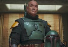 A medium shot of Temuera Morrison as Boba Fett, wearing his green and black Beskar armor without a helmet, standing in his palace on Tatooine.