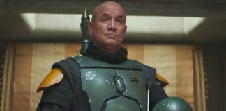 A medium shot of Temuera Morrison as Boba Fett, wearing his green and black Beskar armor without a helmet, standing in his palace on Tatooine.
