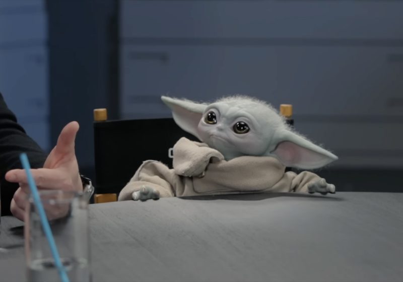 A close-up of the Grogu animatronic puppet sitting at a roundtable during a promotional interview for The Mandalorian and Grogu.