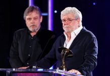 George Lucas holds a gold Saturn Award at a podium while Mark Hamill stands behind him on stage.