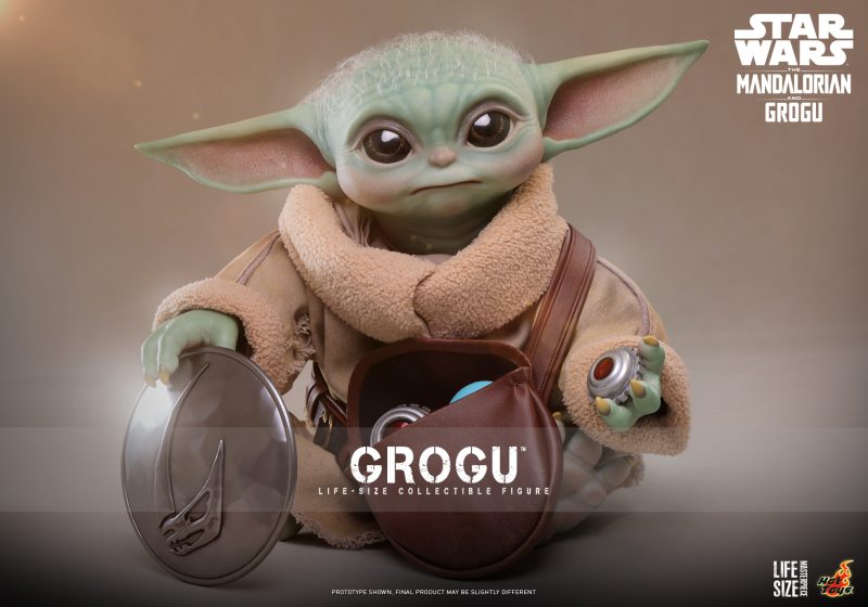 A highly detailed, 1:1 scale Grogu Life-Size Collectible Figure by Hot Toys, featuring a realistic head sculpt, fabric robes, and a leather-like pouch filled with accessories like a magnetic rondel and grav charges.