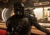 The Mandalorian and Grogu Runtime: How Long is the New Star Wars Movie? The Mandalorian wearing his shiny silver Beskar armor and helmet with the small, green, large-eared Grogu sitting on his right shoulder inside a dimly lit cantina.