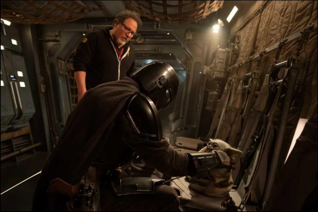 Jon Favreau stands behind Din Djarin and Grogu on a practical set for the upcoming Star Wars movie.