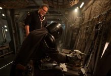 Jon Favreau stands behind Din Djarin and Grogu on a practical set for the upcoming Star Wars movie.