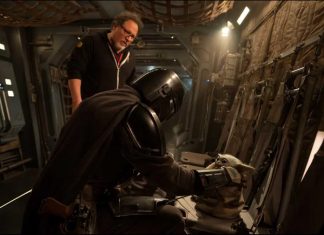 Jon Favreau stands behind Din Djarin and Grogu on a practical set for the upcoming Star Wars movie.