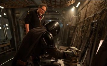 Jon Favreau stands behind Din Djarin and Grogu on a practical set for the upcoming Star Wars movie.
