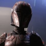 A close-up of a Mandalorian warrior wearing weathered, dark red and black armor with a customized helmet featuring Maul-inspired horn patterns and a cracked visor.