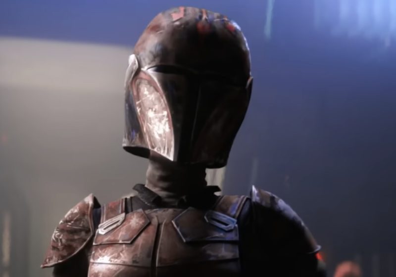 A close-up of a Mandalorian warrior wearing weathered, dark red and black armor with a customized helmet featuring Maul-inspired horn patterns and a cracked visor.