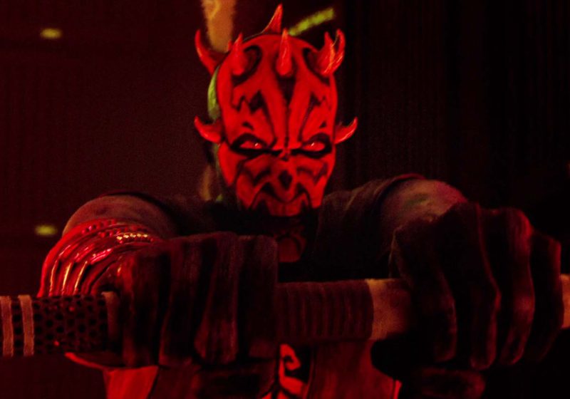 Close-up of Darth Maul with glowing red eyes, gripping a lightsaber hilt in a dark, atmospheric setting from the Star Wars: Maul Shadow Lord series.