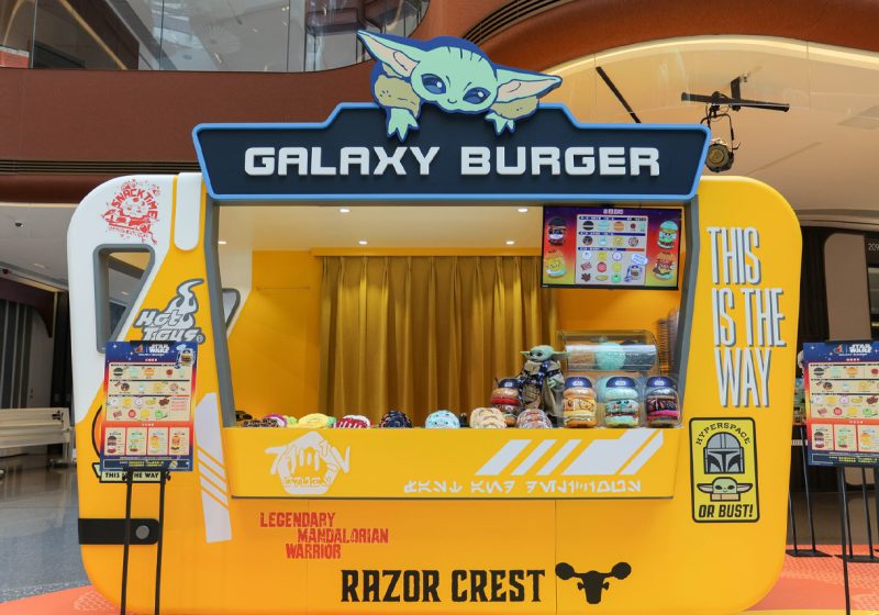 A vibrant yellow "Galaxy Burger" interactive booth designed like the Razor Crest ship, featuring a cartoon Grogu on top and Star Wars-themed menu items at the AIRSIDE Hong Kong exhibition.