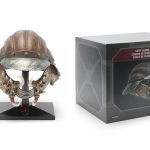 A high-detail replica of Lando Calrissian’s Skiff Guard helmet from Return of the Jedi on a black display stand next to its official Disney packaging.