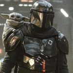 The Mandalorian standing in a dark, industrial setting with Grogu (Baby Yoda) perched on his shoulder, both looking forward.