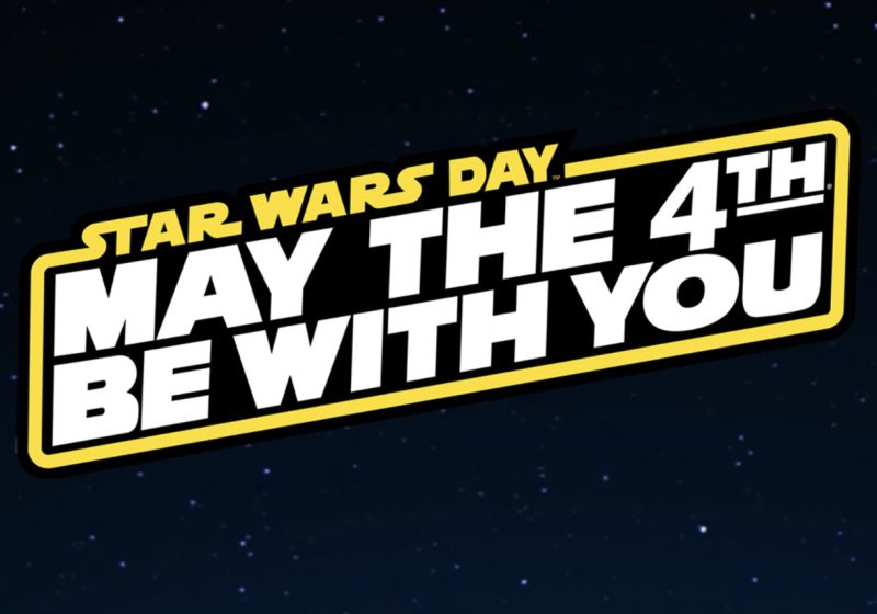 A wide graphic against a dark starry background featuring a bold yellow-bordered plaque with angled text. In smaller yellow text at the top it reads "STAR WARS DAY" and in large white block letters below it reads "MAY THE 4TH BE WITH YOU".