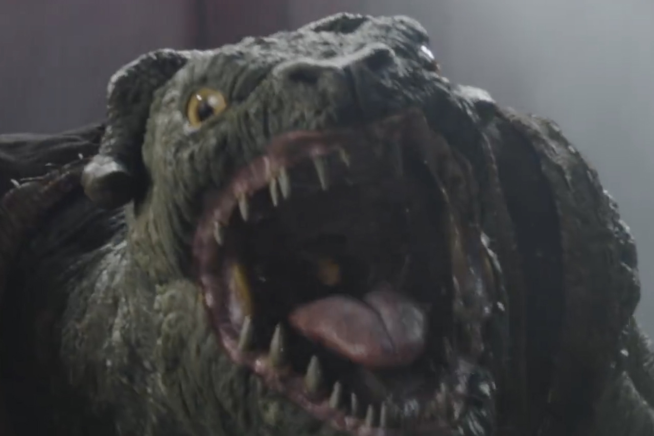 Close-up of a Mantellian Savrip snarling with its mouth wide open, showing sharp teeth and a pink tongue, as seen in The Mandalorian and Grogu TV spot.