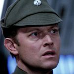 A close-up of Michael Pennington as Moff Jerjerrod in Star Wars: Return of the Jedi, wearing an olive-green Imperial officer's cap and looking off-camera with a concerned expression.