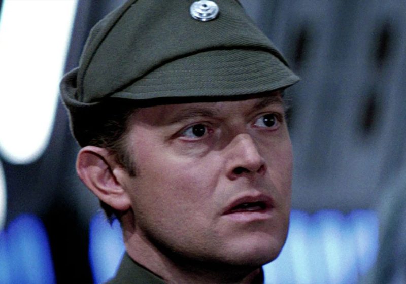 A close-up of Michael Pennington as Moff Jerjerrod in Star Wars: Return of the Jedi, wearing an olive-green Imperial officer's cap and looking off-camera with a concerned expression.