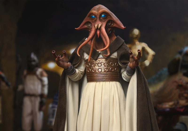 A highly detailed close-up of the Sideshow Tessek Sixth Scale Figure featuring his turquoise eyes, facial tentacles, and ornate bronze belt in a Jabba's Palace setting.